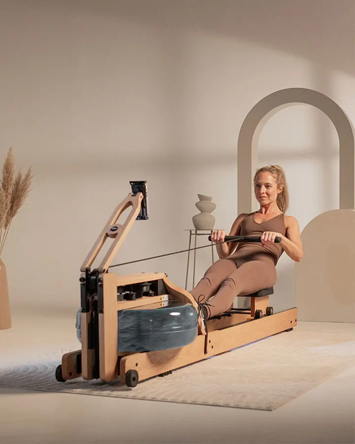 Moteris irkluoja mediniu WaterRower irklavimo treniruokliu šviesioje svetainėje